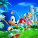 Vibrant promotional image for "Sonic Superstars" featuring Sonic in the foreground with Tails, Knuckles, and Amy in a lush, green environment with iconic loop-de-loops and palm trees in the background, evoking the classic visual style of the original Sonic the Hedgehog games and indicating a return to the series' roots with fast-paced platforming action and beloved characters.