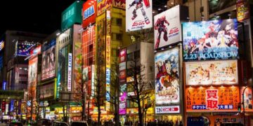 Vista noturna da vibrante Akihabara em Tóquio, iluminada por neons e anúncios de animes, com movimentadas ruas cheias de carros e pedestres