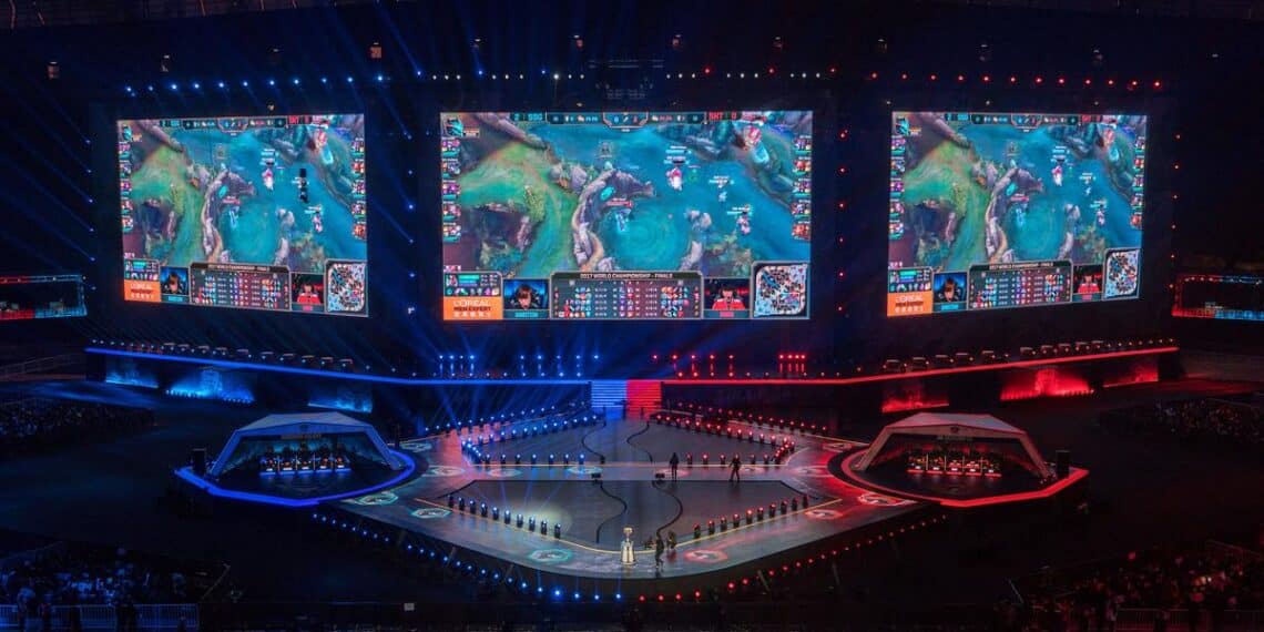 An expansive esports arena engulfs the audience in a spectacular display of competitive gaming, featuring massive screens showing a live League of Legends match Hablamosdegamers