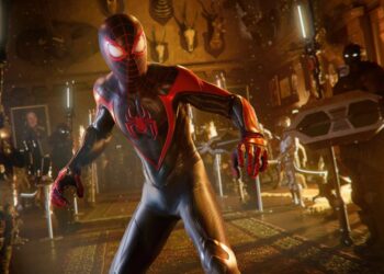 A scene from the Spider-Man 2 game shows Miles Morales in his black and red Spider-Man suit, surrounded by enemies with high-tech gear in a dimly lit room.