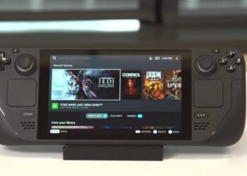 Imagem de alta resolução de uma consola OLED Steam Deck numa mesa de madeira, rodeada de acessórios de jogo, como uma caneca, uma vela e um comando da marca Steam. O ecrã OLED da Steam Deck mostra uma cena de jogo vibrante, realçando a sua qualidade de visualização superior.