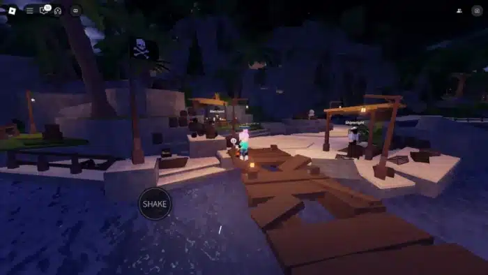 A nighttime Roblox fishing village scene features wooden docks, lanterns, pirate flags, and merchant stalls. A character with pink hair stands on the dock holding a fishing rod, with a "SHAKE" interaction button on screen. NPCs labeled "Merchant" and "Shipwright" are nearby under lamp-lit tents. Palm trees and rocky cliffs surround the area, suggesting a tropical pirate island.