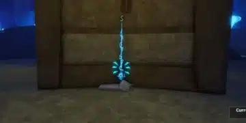 A glowing blue fishing rod is displayed upright on a pedestal inside a dimly lit stone chamber in Roblox. The rod emits a mystical aura, with a green dollar sign hovering above it, indicating its value or purchase option. The environment suggests a hidden or special location, possibly for acquiring rare fishing gear.