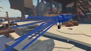 A player in Roblox Fisch stands on a sandy beach beside a large, glowing blue fishing rod with long, tentacle-like extensions, resembling a mythical or cosmic-tier rod. Wooden docks, barrels, and a merchant area are visible in the background.